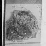 A black and white photo shows an artifact that appears to have a dial on it. There is also some writing on it.